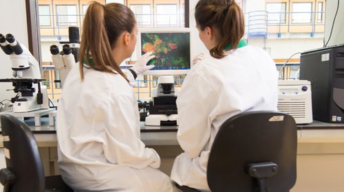 Je ziet twee mensen voor een computer zitten in een laboratorium