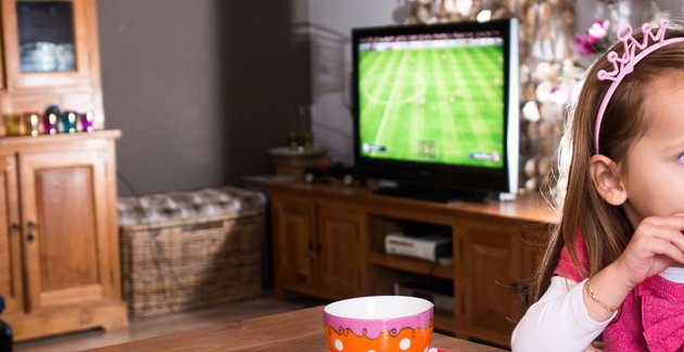Je ziet een kind die een koekje eet met op de achtergrond een vader en broer