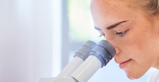Je ziet iemand door een microscoop kijken